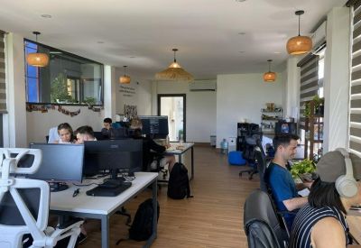 Spacious shared workspace with wooden desks, ergonomic chairs, and warm wicker pendant lights.