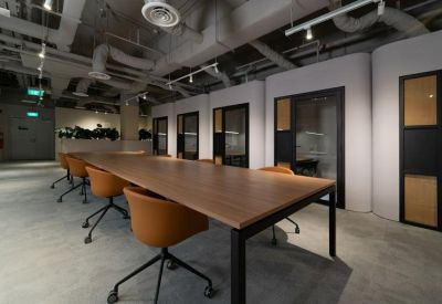 Long communal wooden table with orange chairs in a modern office setting.