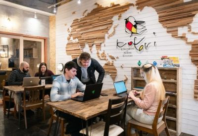 People working at wooden tables in a coworking space with a large world map wall feature.