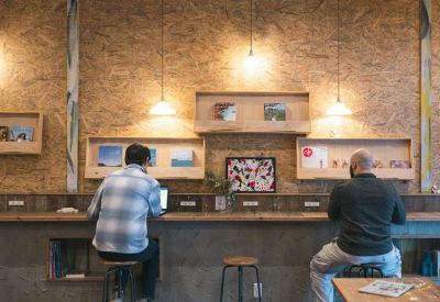 Individuals focused on work at a wooden counter desk equipped with power outlets.