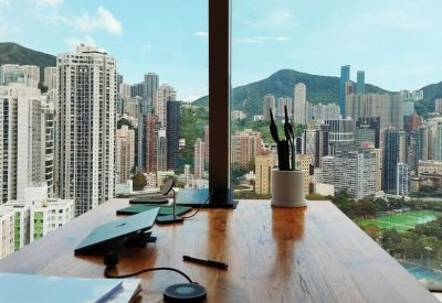 Wooden meeting table with a laptop and plant overlooking a dense urban cityscape.