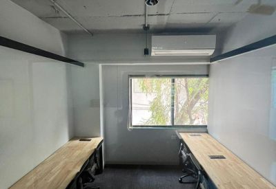 Long wooden workstations in a bright office with a large window and air conditioning.