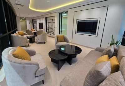 Spacious lounge with curved armchairs, yellow cushions, and a large wall-mounted screen.