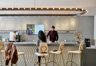 Modern café area featuring a patterned tile wall, sleek grey counter, and stylish white bar stools.
