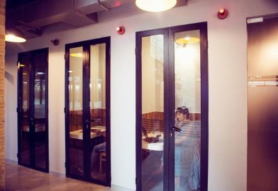 Sleek glass-fronted private phone booths or focus rooms along a brightly lit corridor.