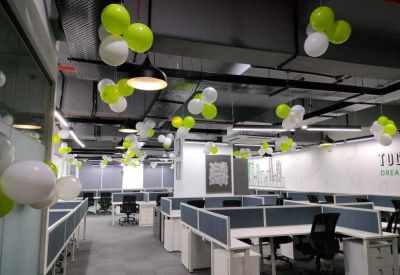 Spacious open-plan office with white desks and green and white balloons hanging from the ceiling.