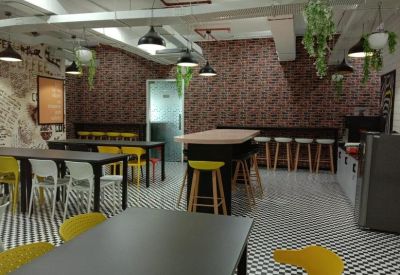 Modern office cafeteria with long tables, yellow stools, and hanging greenery.