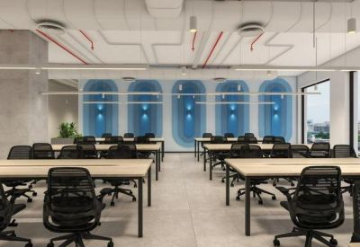 Bright open-plan workspace with rows of wooden desks and black ergonomic chairs.