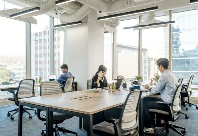 Bright open-plan office featuring wooden desks, ergonomic chairs, and large windows.