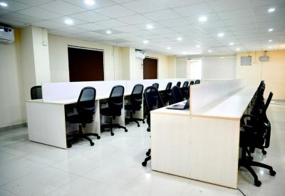 Open-plan workspace with rows of white desks and black ergonomic chairs.