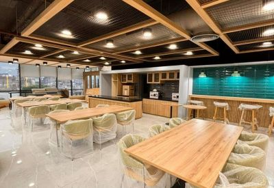 Spacious communal dining area with wood-framed ceiling grids and emerald green tiled backsplash.