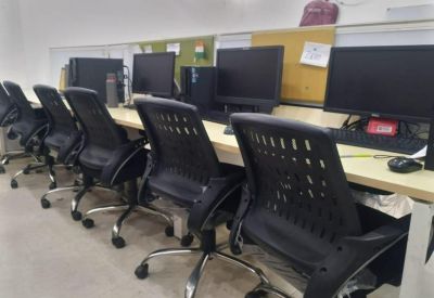 Row of black ergonomic office chairs at a long shared desk with computer monitors.