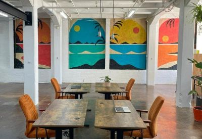 Open-plan workspace featuring wooden standing desks, orange chairs, and vibrant tropical murals.