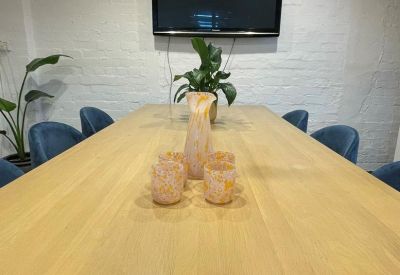 Meeting room with a long light wood table, blue velvet chairs, and a large wall-mounted monitor.