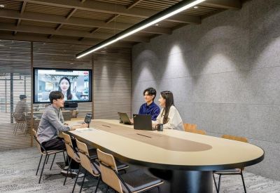 Professional meeting room with an oval wooden table and a video conferencing screen on a textured wall.