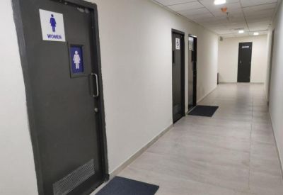 Long office hallway featuring grey doors with restroom signage and white walls.