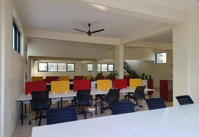 Spacious open-plan office with white desks, colorful dividers, and a ceiling fan.
