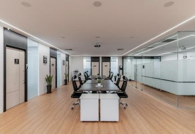 Bright coworking space with long wooden tables and black ergonomic chairs.