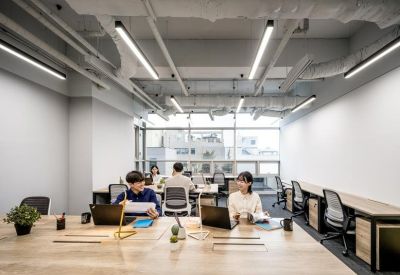 Bright coworking space with long wooden tables, ergonomic chairs, and industrial ceiling details.