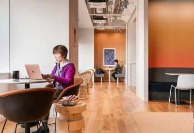Sunny breakout area with wood flooring, café seating, and a colorful orange gradient wall.