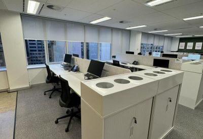 Bright open-plan office space with white desks, ergonomic black chairs, and large windows.