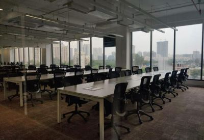 Open-plan office with rows of desks, ergonomic chairs, and large windows overlooking the city.