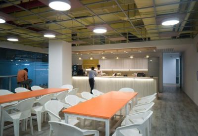 Modern cafeteria area with orange tables, white chairs, and a sleek serving counter.