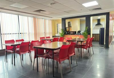 Spacious communal dining area with red chairs, wooden tables, and a kitchen visible in the background.