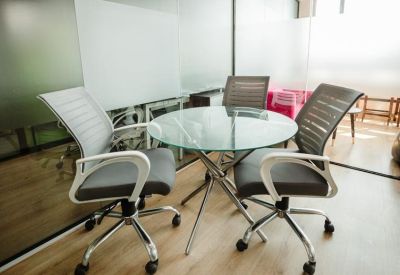 Small glass-topped breakout table with four modern grey office chairs.