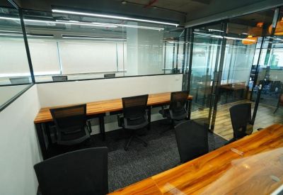 Modern workspace with a continuous wooden desk along a glass wall and ergonomic black chairs.