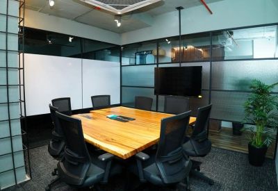 Symmetrical meeting room with a natural wood table, black chairs, and a wall-mounted screen.