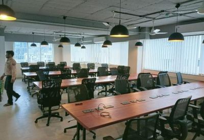 Large open-plan workspace featuring multiple rows of wooden desks and black mesh chairs.