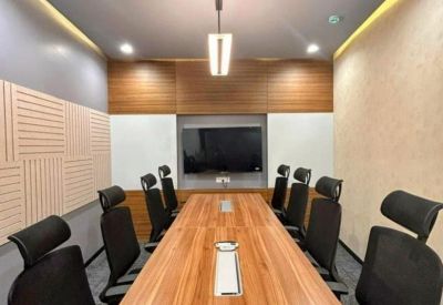 Professional boardroom with a long wooden table, ergonomic black chairs, and a large wall-mounted screen.