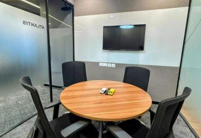 Small meeting room with a round wooden table, four black chairs, and a wall-mounted television.