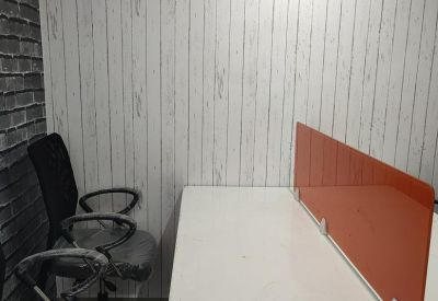 Two-person desk setup against a light wood paneled wall with a grey brick accent.