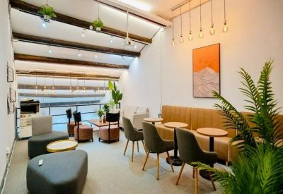 Bright communal lounge with a plush tan banquet, cafe tables, and colorful abstract wall art.