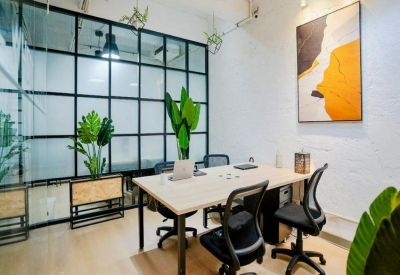 Private glass-walled office suite featuring a light wood desk, vibrant green plants, and modern art.