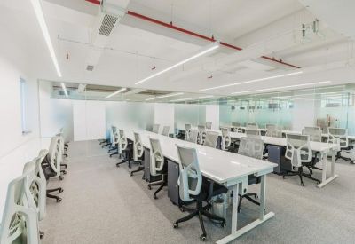 Bright open-plan office with rows of white desks and ergonomic grey chairs.