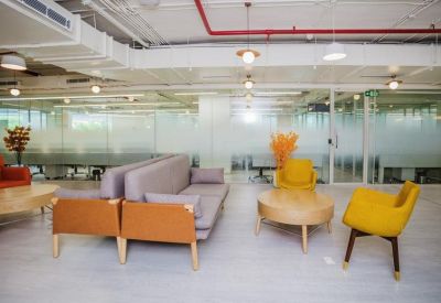Bright breakout area with grey sofas, yellow armchairs, and round wooden coffee tables.