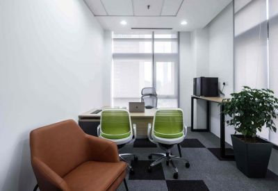Private office suite featuring two green chairs, a wooden desk, and a large potted plant by the window.
