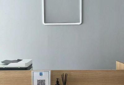 Minimalist reception area with a wooden front desk, QR code sign, and a square light fixture on a grey wall.