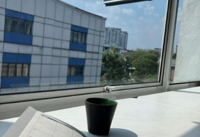 Close-up of a notebook and coffee mug on a white desk overlooking an urban view through large windows.