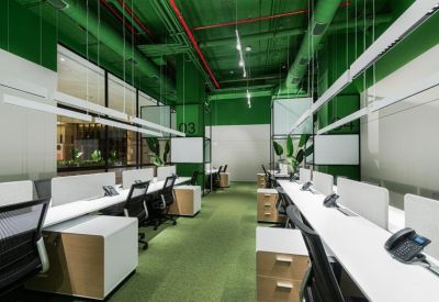 Modern open-plan office with white desks, ergonomic chairs, and vibrant green walls.