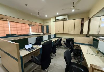 Modern coworking space with multiple desk stations, laptops, and a ceiling fan.