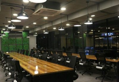 Large open-plan workspace with long wooden desks, industrial lighting, and a green plant wall.