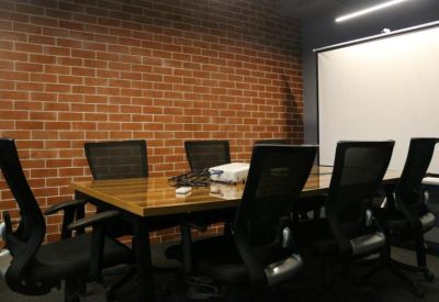 Meeting room with a large wooden table, mesh chairs, and a projector screen against a brick wall.