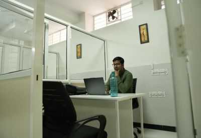 Private glass-partitioned office suite with a man working at a white desk with a laptop.