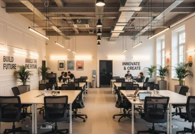 Spacious open-plan coworking space with long wooden tables and black ergonomic chairs under industrial lighting.
