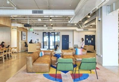 Bright coworking lounge with leather sofas, green armchairs, and colorful geometric rugs.