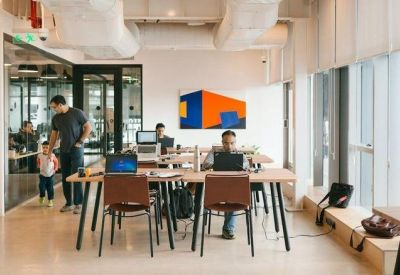Bright open-plan workspace with wooden desks, ergonomic chairs, and colorful abstract wall art.